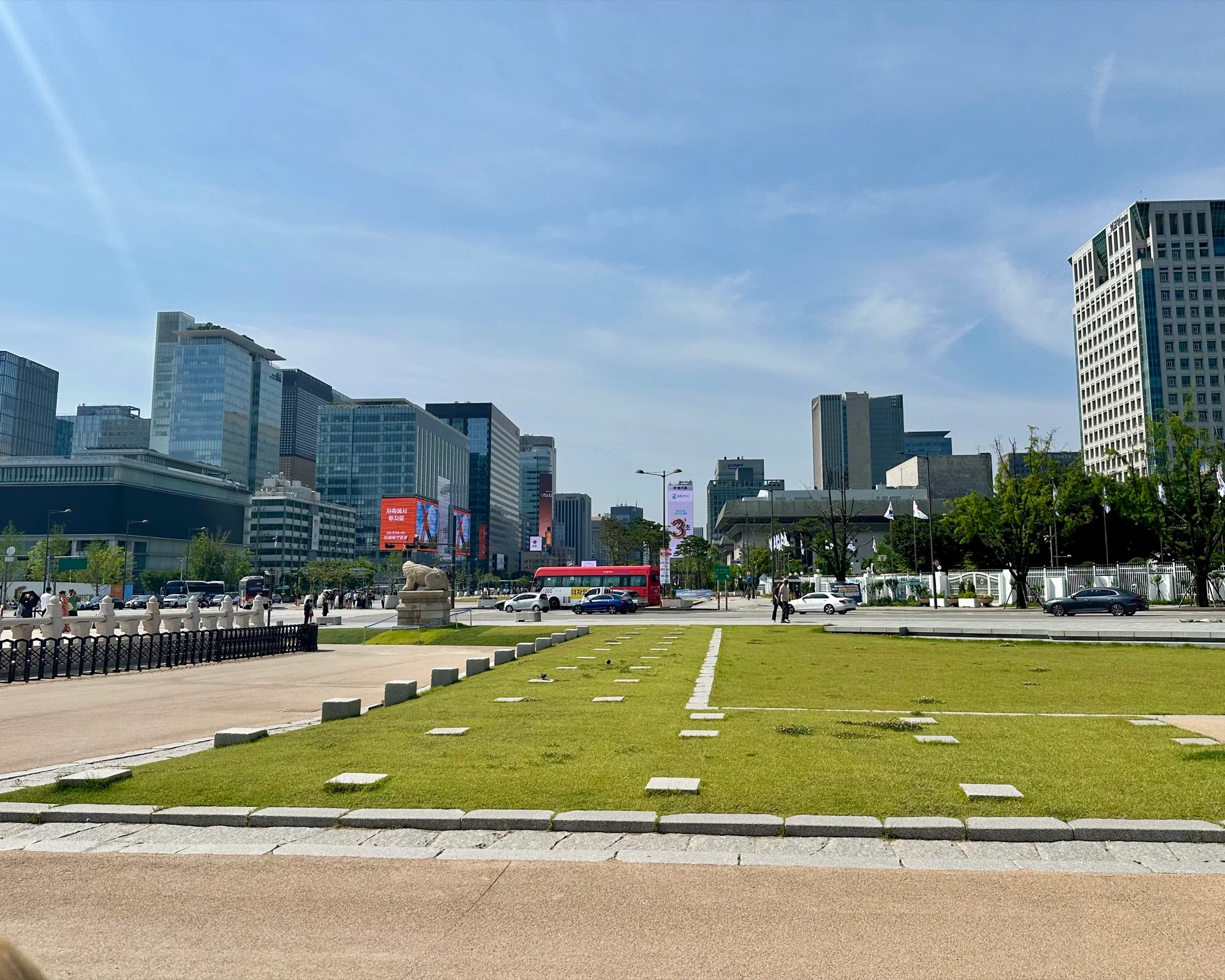 Gwanghwamun Square looking south from the palace, a lawn and stone haetae statue in front of the modern Seoul skyline of skyscrapers.